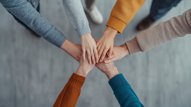 Diverse group of people placing hands together in a show of unity and teamwork.