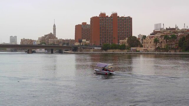 Small tourist motorboat cruising on the water of the nile river in cairo, with the city skyline and cairo tower visible on the bank