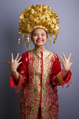 Fototapeta premium Smiling Indonesian Asian Girl in Red and Gold Traditional Ceremonial Costume With Ornate Golden Headdress