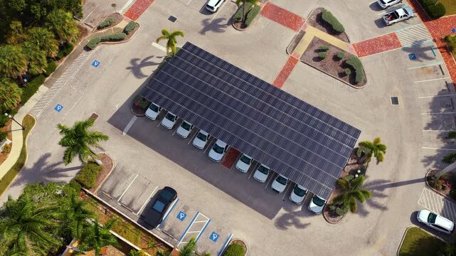Solar power generation technology integrated in urban infrastructure. Photovoltaic panels installed as shade roof over parking lot with parked cars for effective production of clean energy.