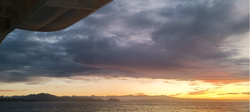 Sunrise over mountains, sea, and city with a glowing orange sky.