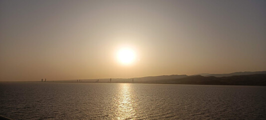 Fototapeta premium Sunrise over mountains, sea, and city with a glowing orange sky.