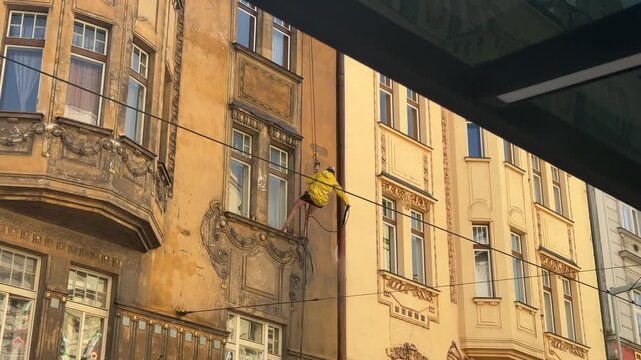 A worker rappelling down an aged ornate building exterior, performing window cleaning service, using specialized rope access equipment, demonstrating skilled professional labor, urban maintenance.