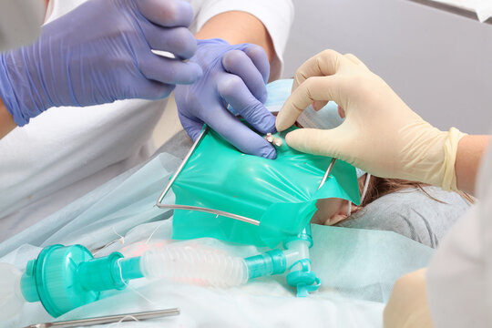 Installing cofferdame for child. Cofferdam is in dentist's hands. Treatment of baby teeth under anesthesia. An open mouth. Breathing tube in baby's mouth. Modern dentistry.