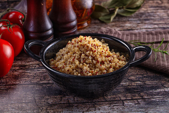 Healthy cooked tri-color quinoa in a bowl with fresh tomatoes and rosemary on a rustic wooden table