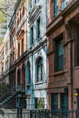 Fototapeta premium A sunny street-level view of classic, historic brownstone townhouses in Manhattan, New York City, featuring ornate architecture and traditional details.