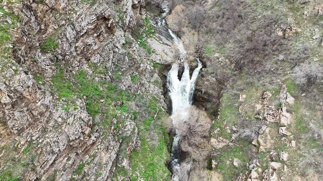 4K aerial drone footage of cascading waterfall in rocky mountain canyon, flowing stream through natural landscape.