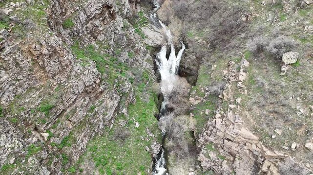 4K aerial drone footage of cascading waterfall in rocky mountain canyon, flowing stream through natural landscape.