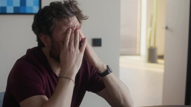 Medium close up of exhausted middle aged male Caucasian writer rubbing eyes and head after long hours of work on laptop
