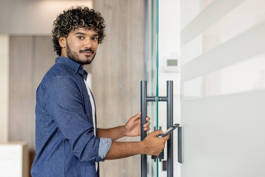 Portrait of a young Indian man opening the door to a room with his phone and looking into the camera
