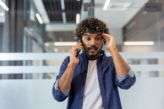 Close-up photo of a young Indian man talking on the phone in a shocked manner in the office