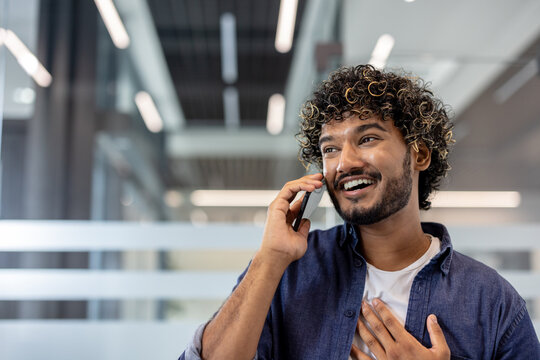 Close-up photo of a young Indian man talking on the phone in an office and looking to the side