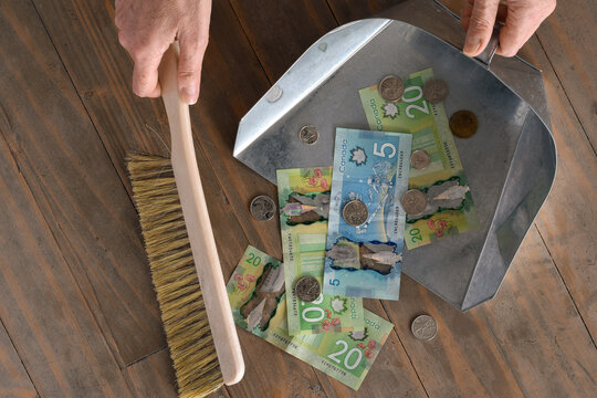 Hands sweeping Canadian dollar bills from floor into dustpan, symbolizing financial loss, rising expenses, debt, or cost of living pressure. Concept image for inflation, recession, taxes, or money man
