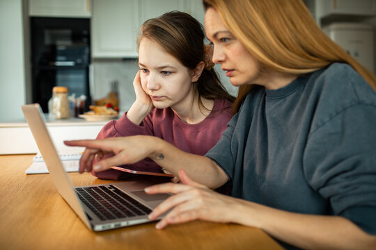 Mother helping teenage daughter with homework on laptop at kitchen table