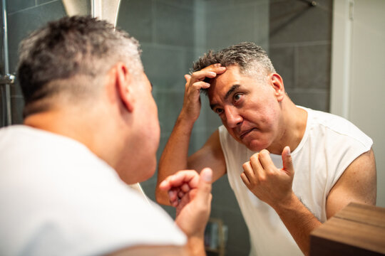 Middle-aged man checking hair loss in bathroom mirror