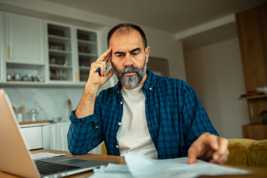 Middle-aged man reviewing bills in home kitchen