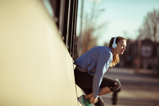 Young woman runner stretching with headphones on city street