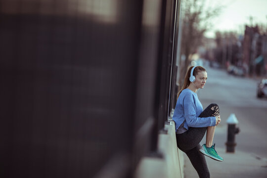 Young woman runner resting with headphones on city sidewalk
