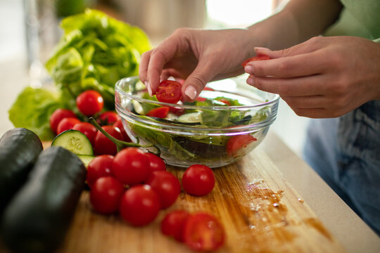 Person preparing fresh tomato cucumber salad at home kitchen