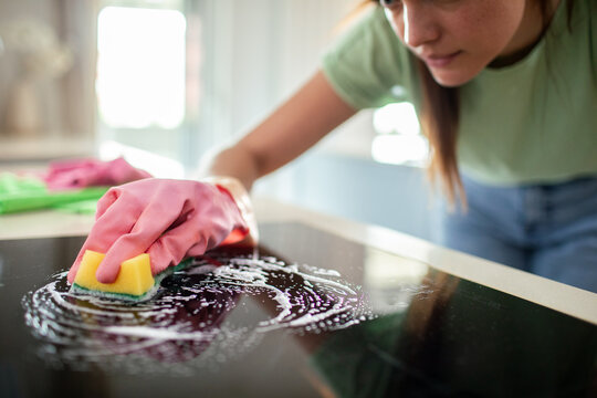 Woman scrubbing glass stovetop with sponge in home kitchen