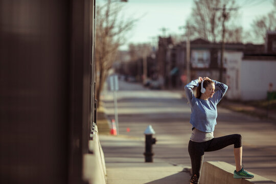 Young woman warming up for run with headphones on city street
