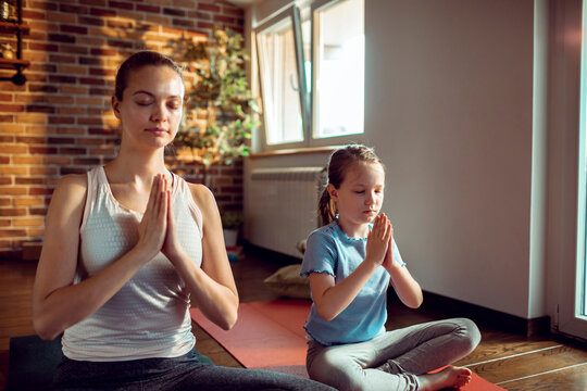 Mother and daughter meditating together on yoga mats at home