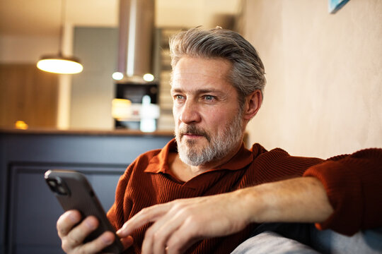 Mature man using smartphone on couch at home