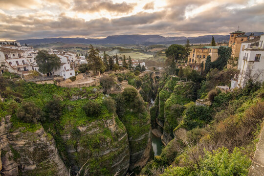 Breathtaking aerial view of Ronda's deep limestone canyon and traditional white houses at sunset. Perfect for Mediterranean travel, history, and European tourism content.