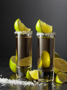 Tequila shots with salt and lime slices on a black stone table.