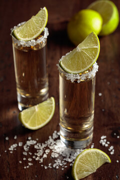 Tequila with salt and lime slices on an old wooden table.