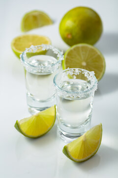 Tequila with salt and lime slices on a white table.
