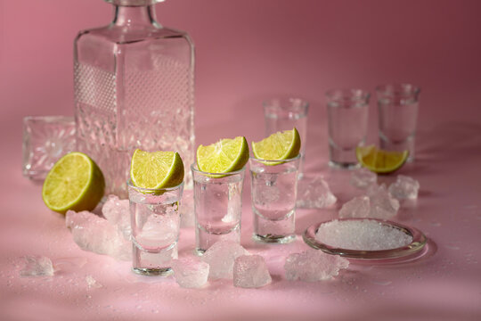 Tequila with lime, sea salt, and crushed ice on a pink background.