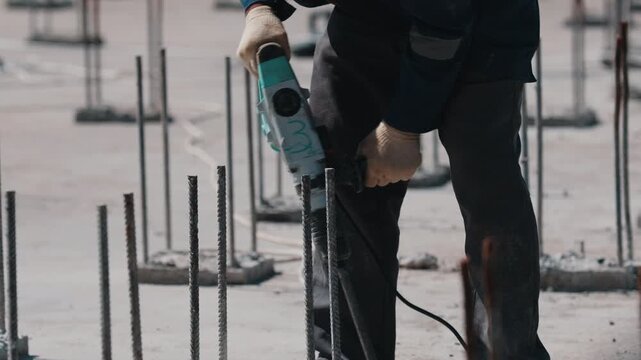 Worker breaking concrete with jackhammer around rebar at construction site