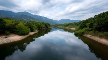 Obraz premium A calm river flows through lush green valleys perfectly reflecting a dramatic cloudy sky beneath layered mountains