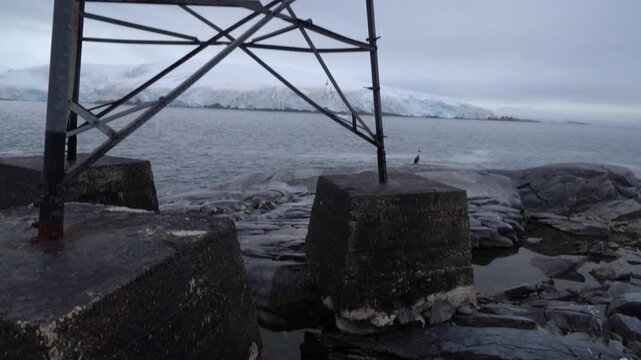 Panning down from the base of a metal radio tower at Argentina's Melchior Base to the rocky shoreline and cold waters of the Dallmann Bay in Antarctica
