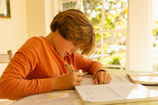 12 year old boy doing homework at kitchen table at sunset