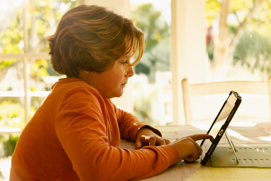 12 year old boy using tablet at home at sunset
