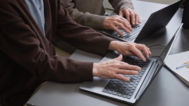 Top view shot of two unrecognizable senior people man and woman using laptops at desk in school classroom with focus on hands typing on keyboard, copy space
