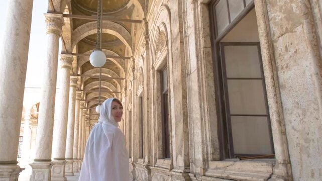 A tourist woman in white walks through a historic mosque corridor in Cairo, Egypt, captured in slow motion full HD during travel.