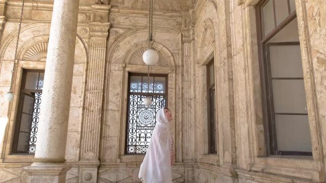 A female tourist stands by an ornate window inside a historic mosque in Cairo, Egypt, captured in slow motion full HD during travel.