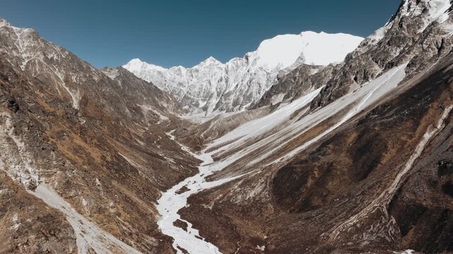 Aerial drone view of a dramatic Himalayan valley with snow-covered peaks rising above rugged terrain in Nepal.