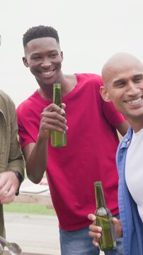 Vertical video: Clinking green beer, three friends leaning, viewing phone at picnic, showing spoons