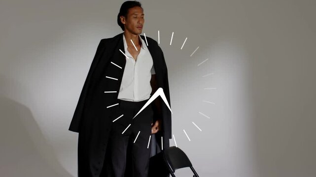 Vertical video: Male model swinging coat open on fashion set, draping and timing poses to clock
