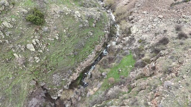 4K aerial drone footage of rocky mountain terrain with stream flowing through canyon, natural landscape background.