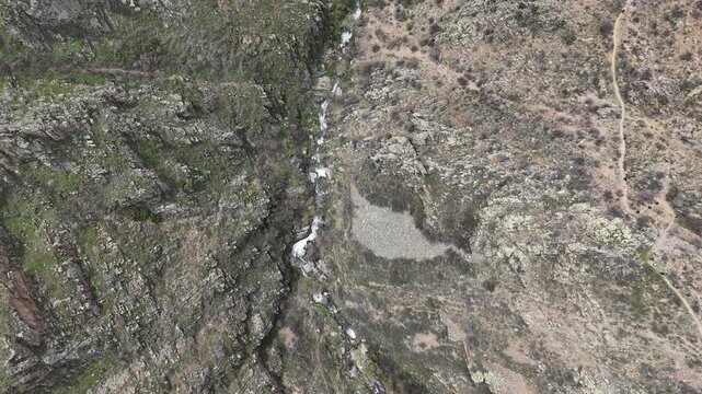 4K aerial drone footage of rocky mountain terrain with stream flowing through canyon, natural landscape background.