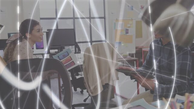 Woman pointing swatch, making man tapping tablet in design office, light streaks showing palette