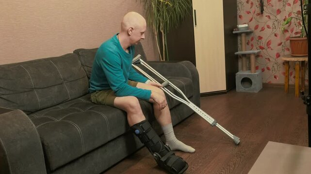 Man adjusting crutches height while sitting on sofa, recovery preparation, rehabilitation and mobility support concept.