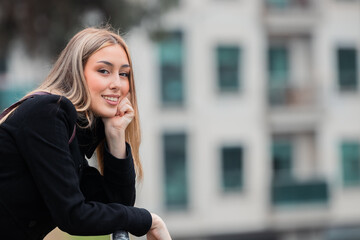 Fototapeta premium beautiful young woman leaning against the street looking at the camera, smiling, with copy space