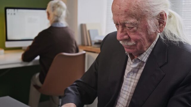Tilt up shot of senior man with moustache looking down on laptop screen while attending computer class for seniors and using internet in school, copy space
