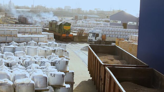 An open freight car loaded with bulk materials moves through an outdoor factory warehouse. Industrial rail freight transportation. Transportation of clay and sand in open rail cars.